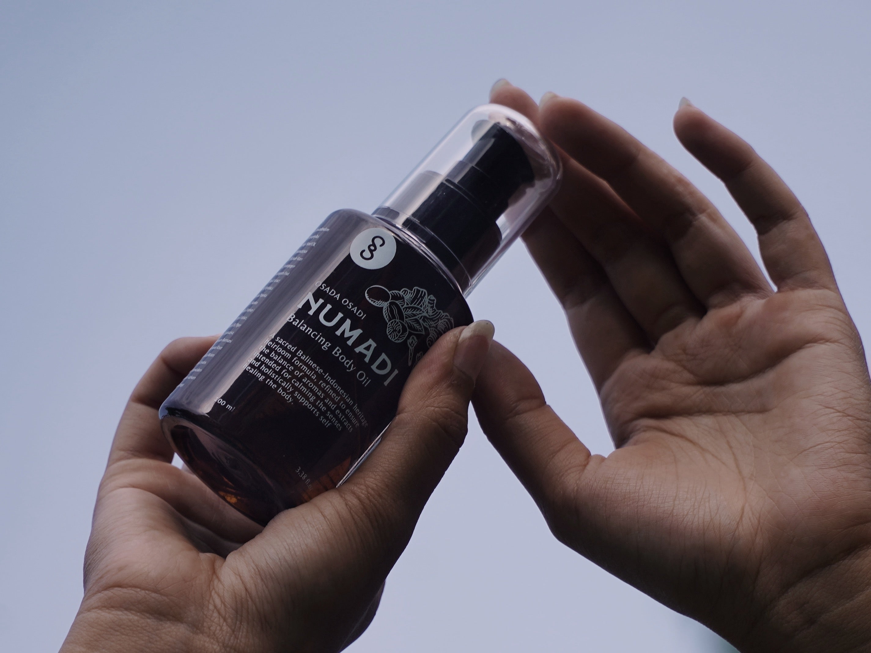 A pair of hands hold onto OSADA OSADI's natural balancing body oil, Numadi.